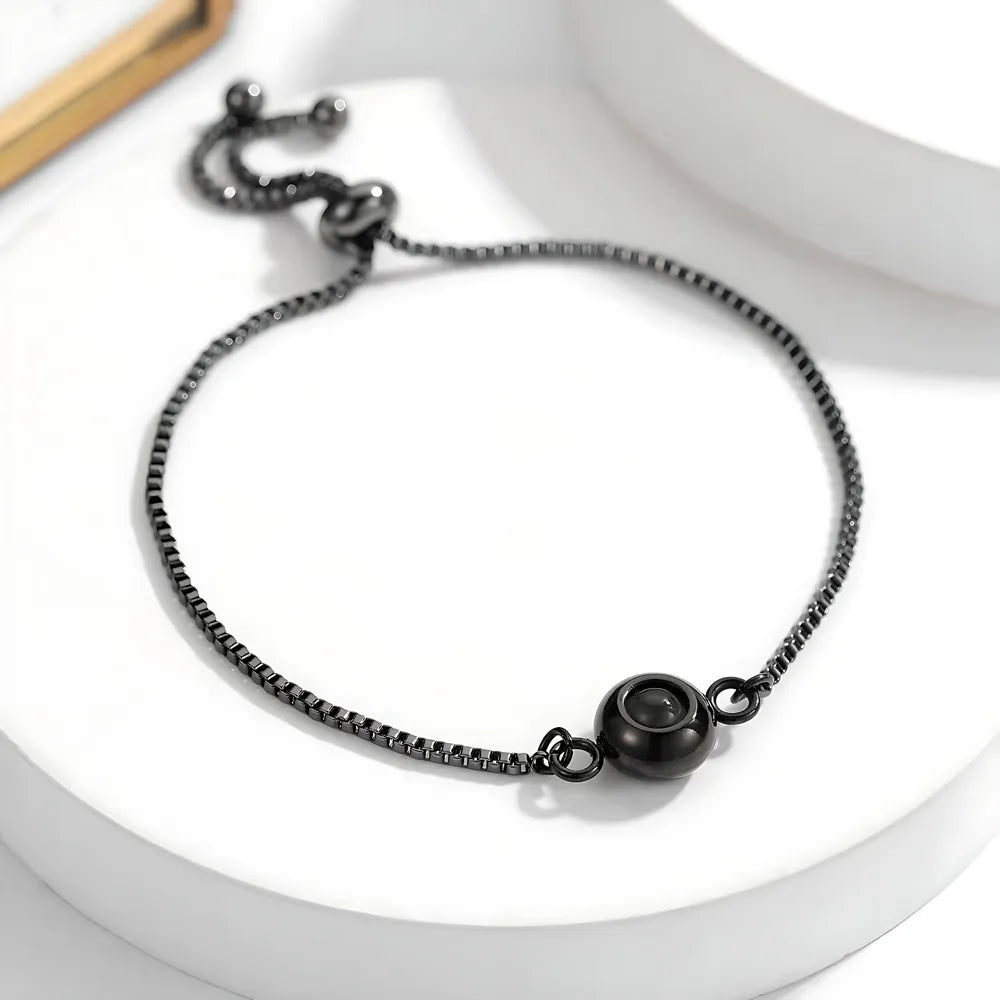 Black chain photo projection bracelet with a round clasp on a white surface