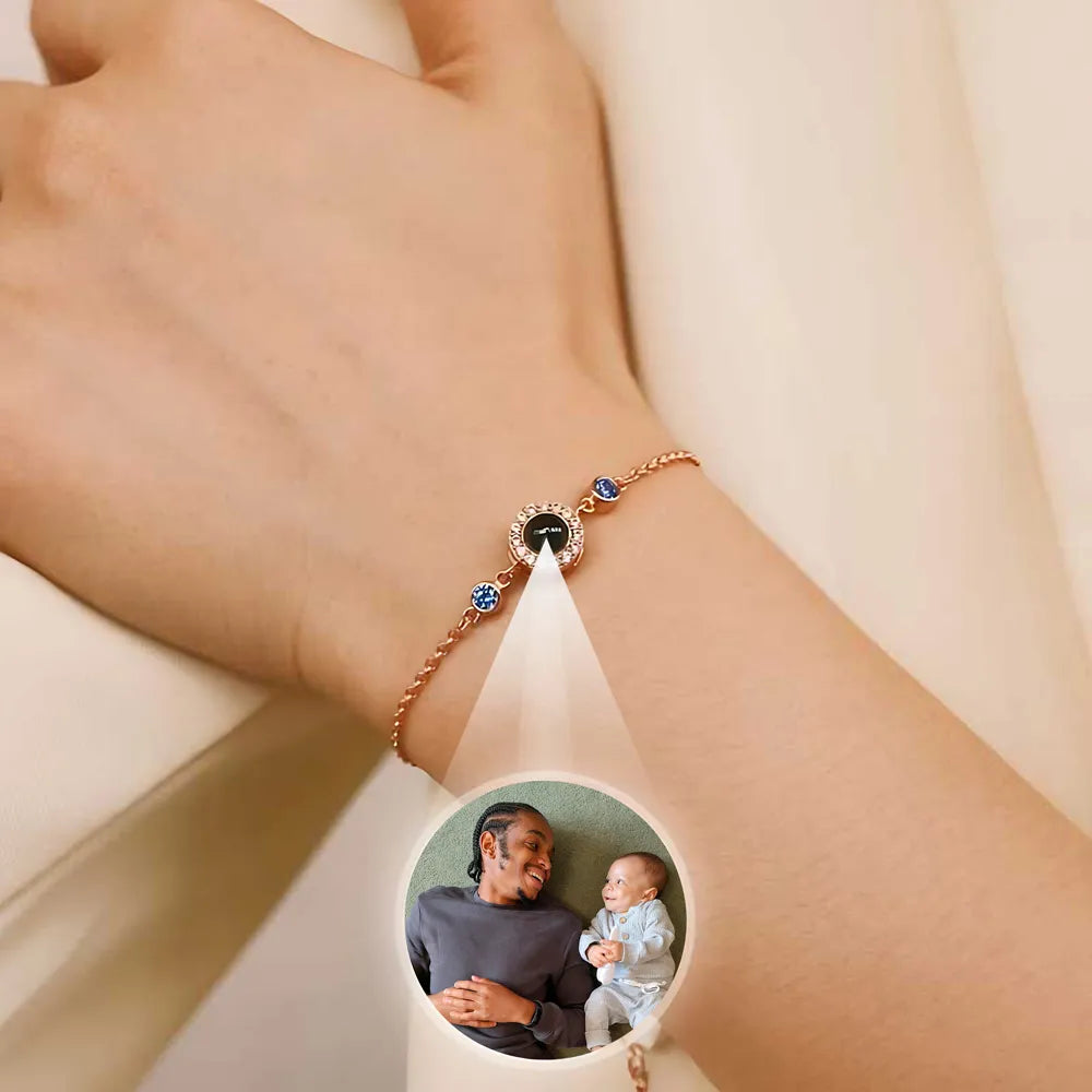 Bracelet with a round charm featuring a photo of a woman and a baby, worn on a wrist.